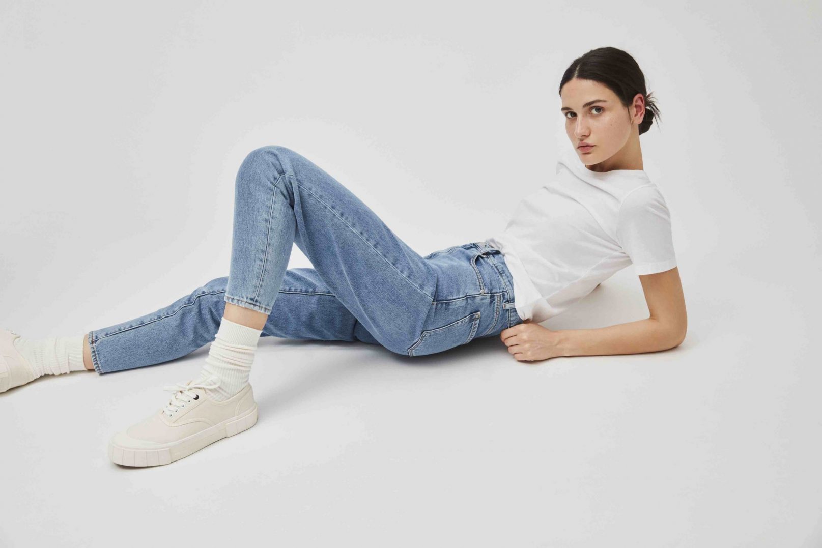 Frau liegt auf dem Boden mit Jeans weißem Shirt Sneakern und weißen Strümpfen