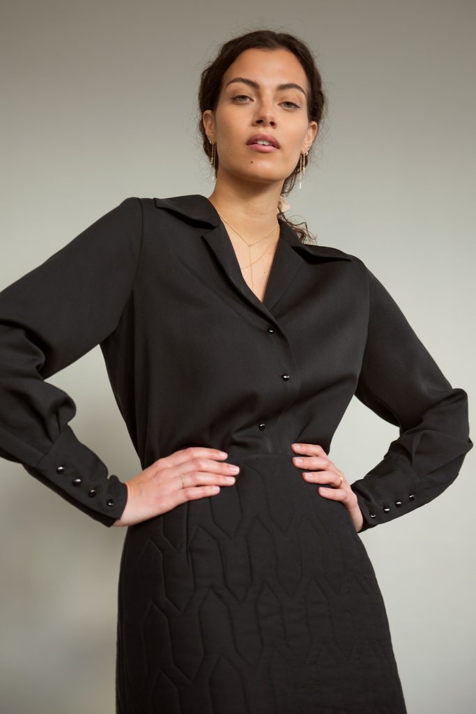 Fair Fashion Junge Frau mit dunklen Haaren trägt eine schwarze Bluse und einen schwarzen Stepprock. Beides vegane Mode